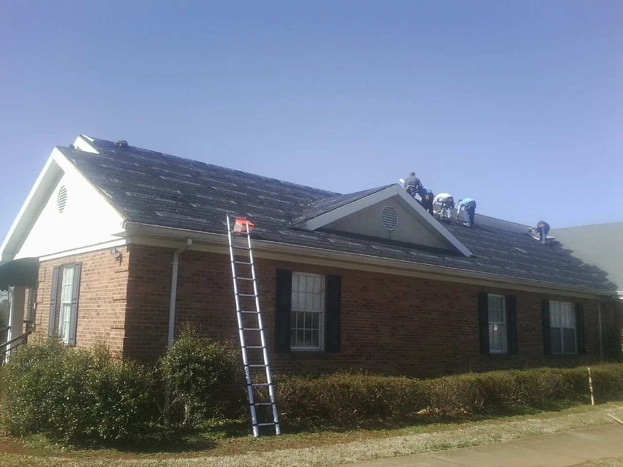 Crew tearing shingles off a brick ranch roof with a ladder set — Emergency Roof Repair work by our crew in Connersville