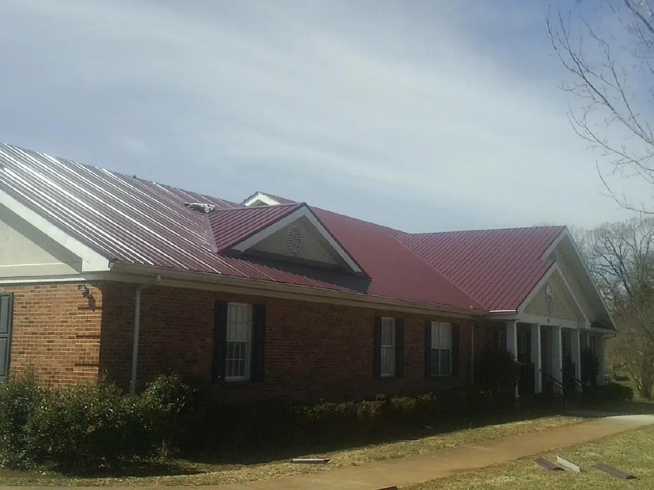 Red metal roof with gabled entries on a long brick building, from a Hail Damage Roof Repair job in Connersville