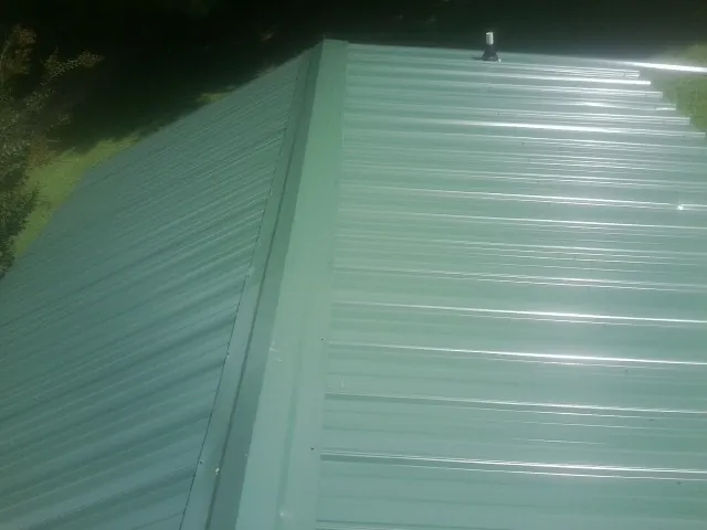 New green metal panels meeting at the ridge of a roof — Flat Roof Repair work by our crew in Connersville