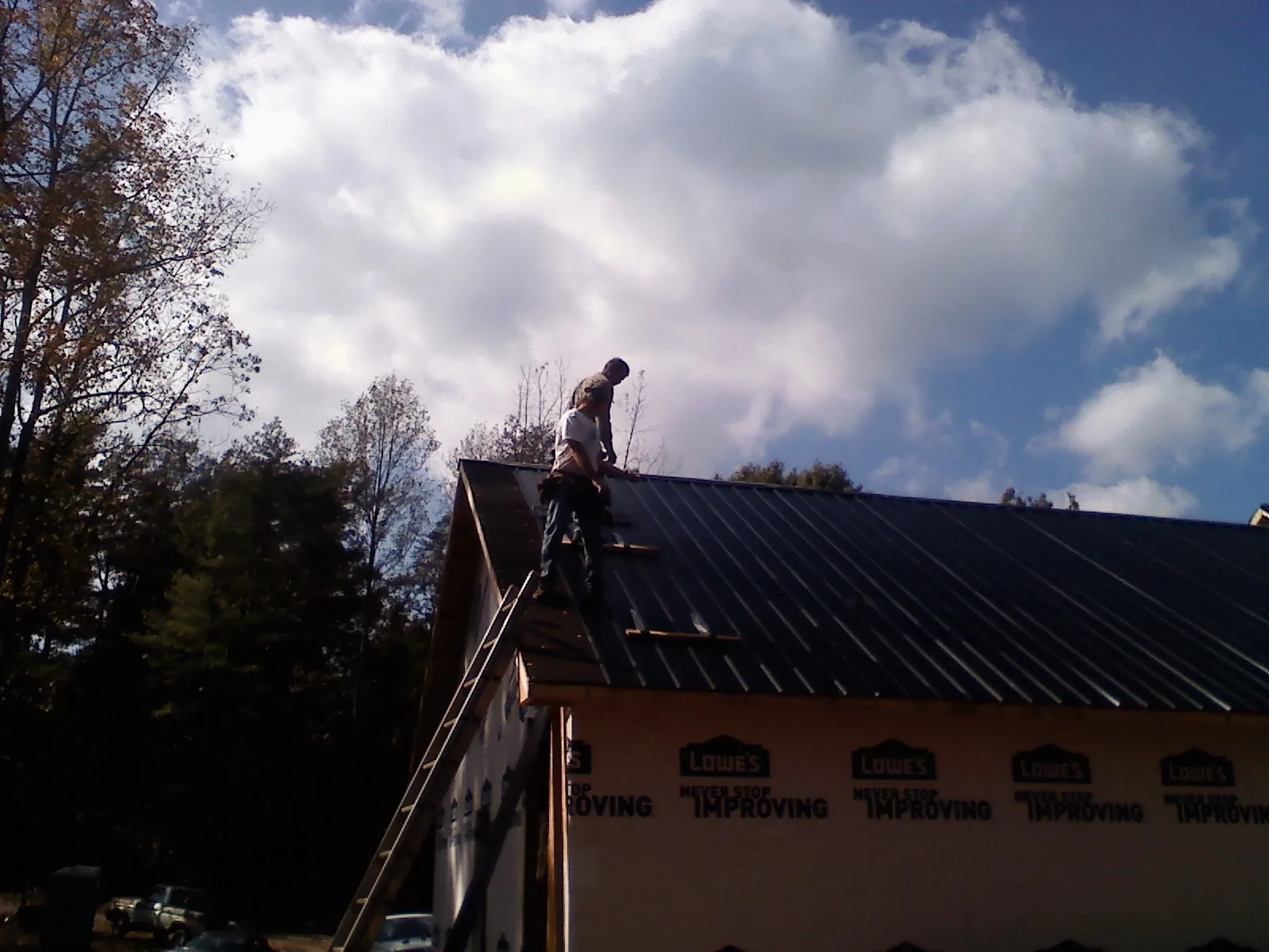Roofer fastening dark metal panels high against a cloudy sky, from a Roof Inspection job in Connersville