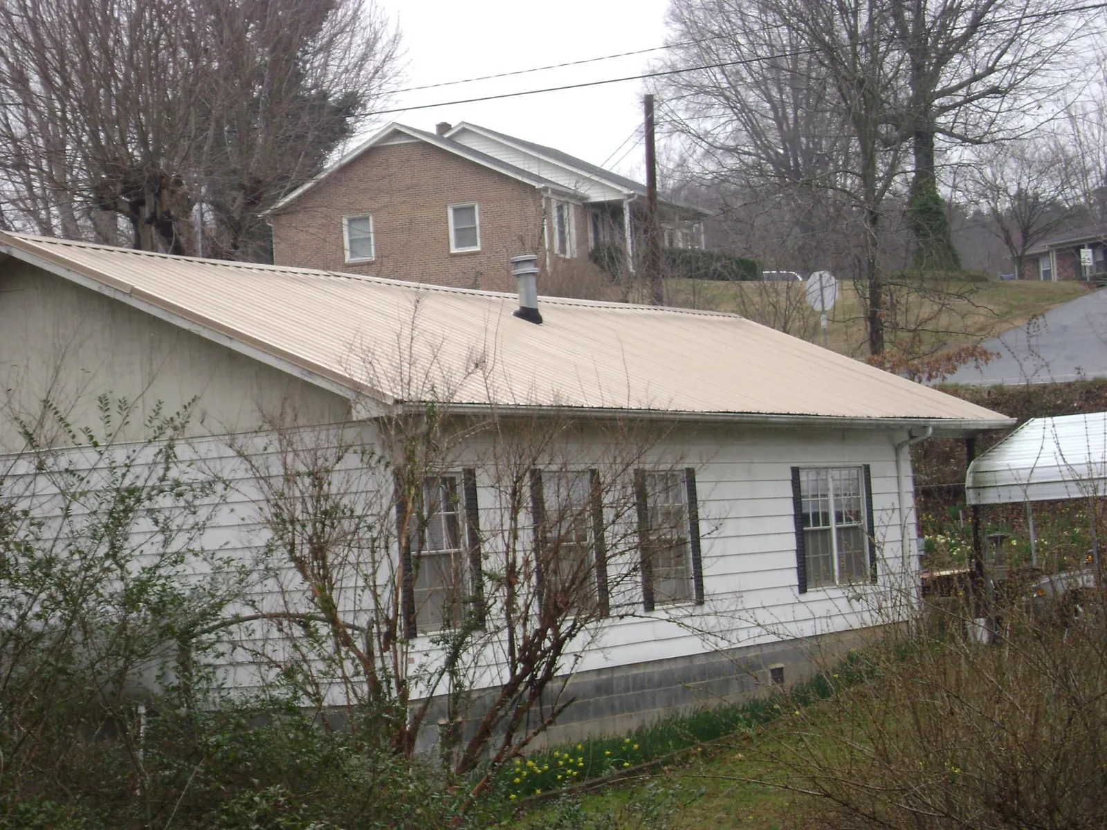 Tan metal roof on a white sided house set into a hillside — Commercial Roofing by Roofing Brothers in Connersville
